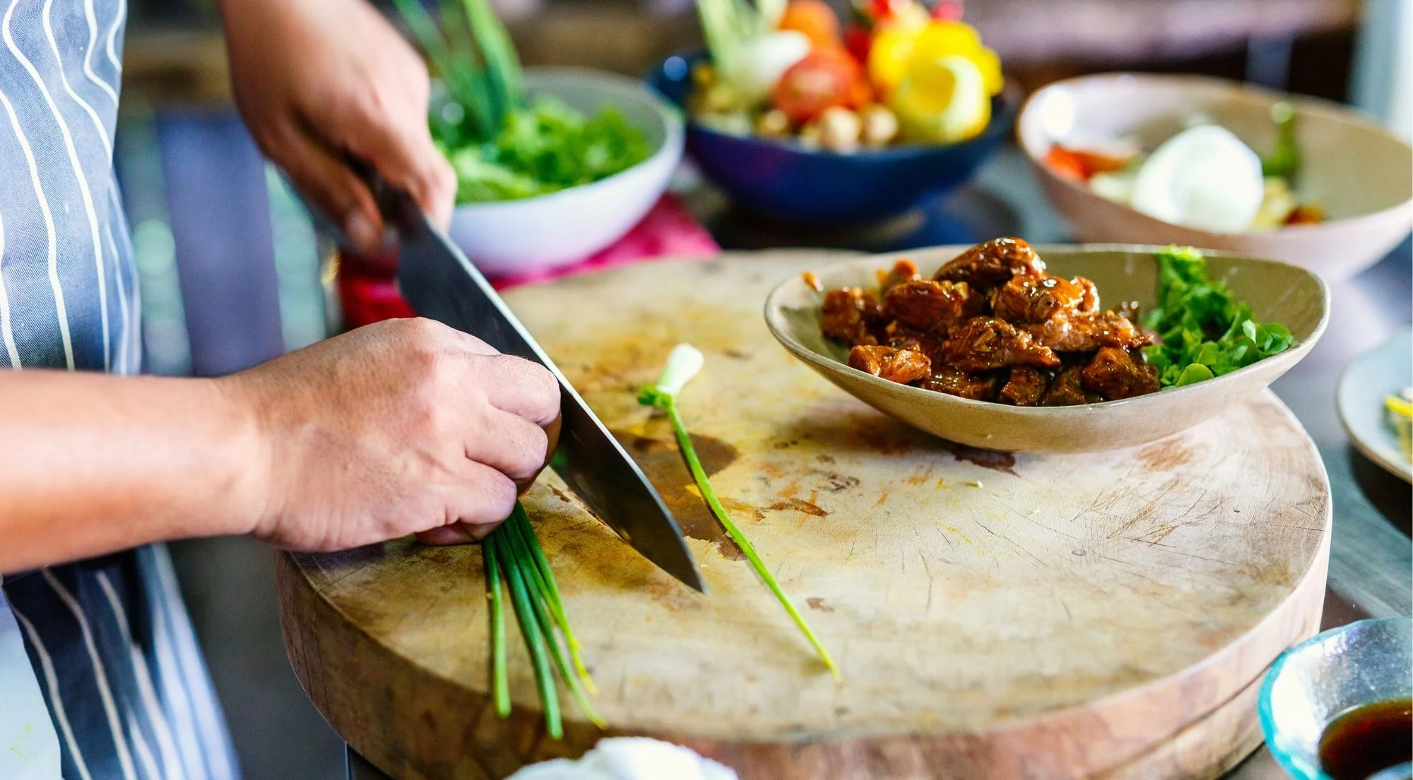 Chef chopping fresh herbs on a wooden cutting board surrounded by colourful vegetables
