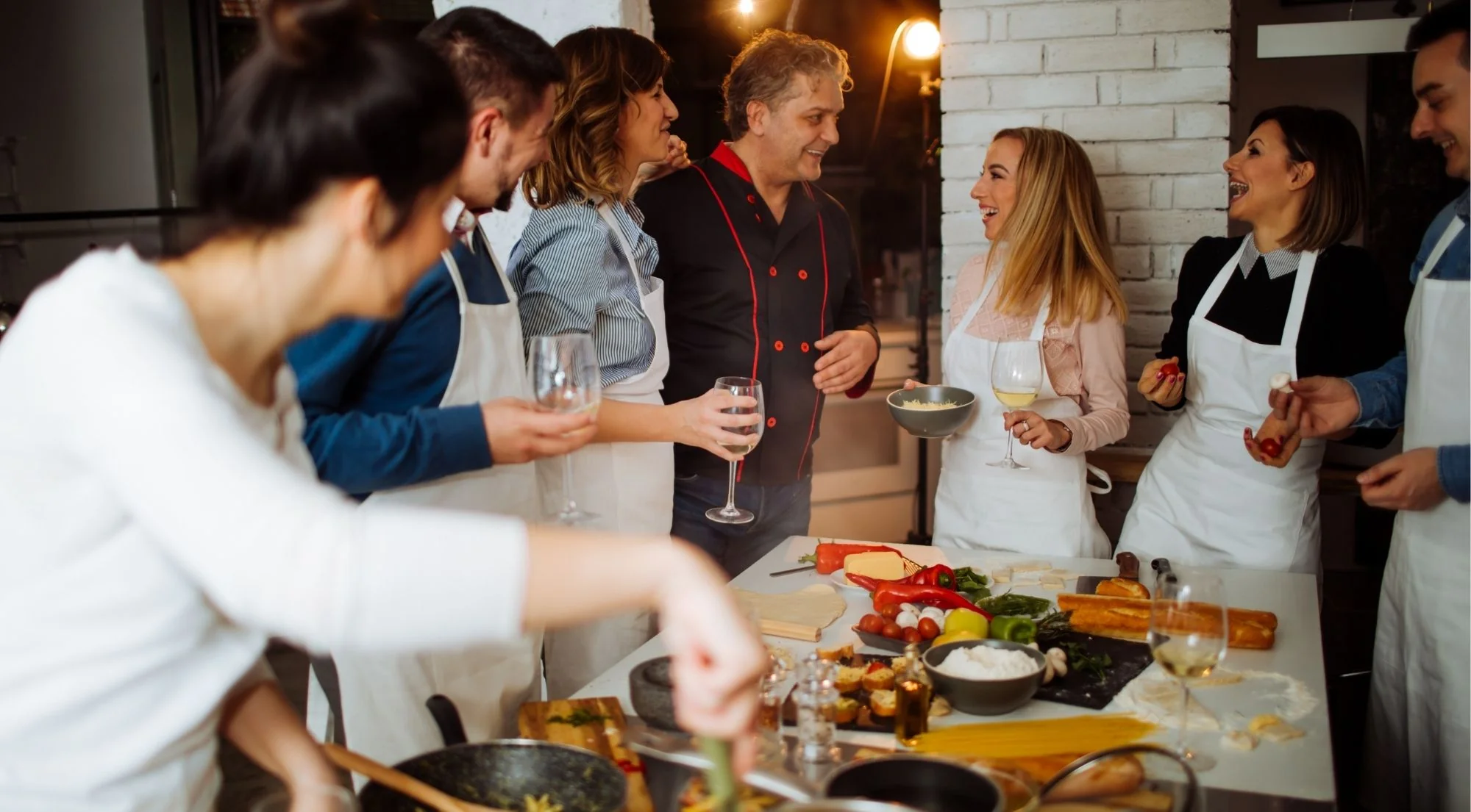 Happy group of cooking class participants with chef and glasses of wine in a warm kitchen